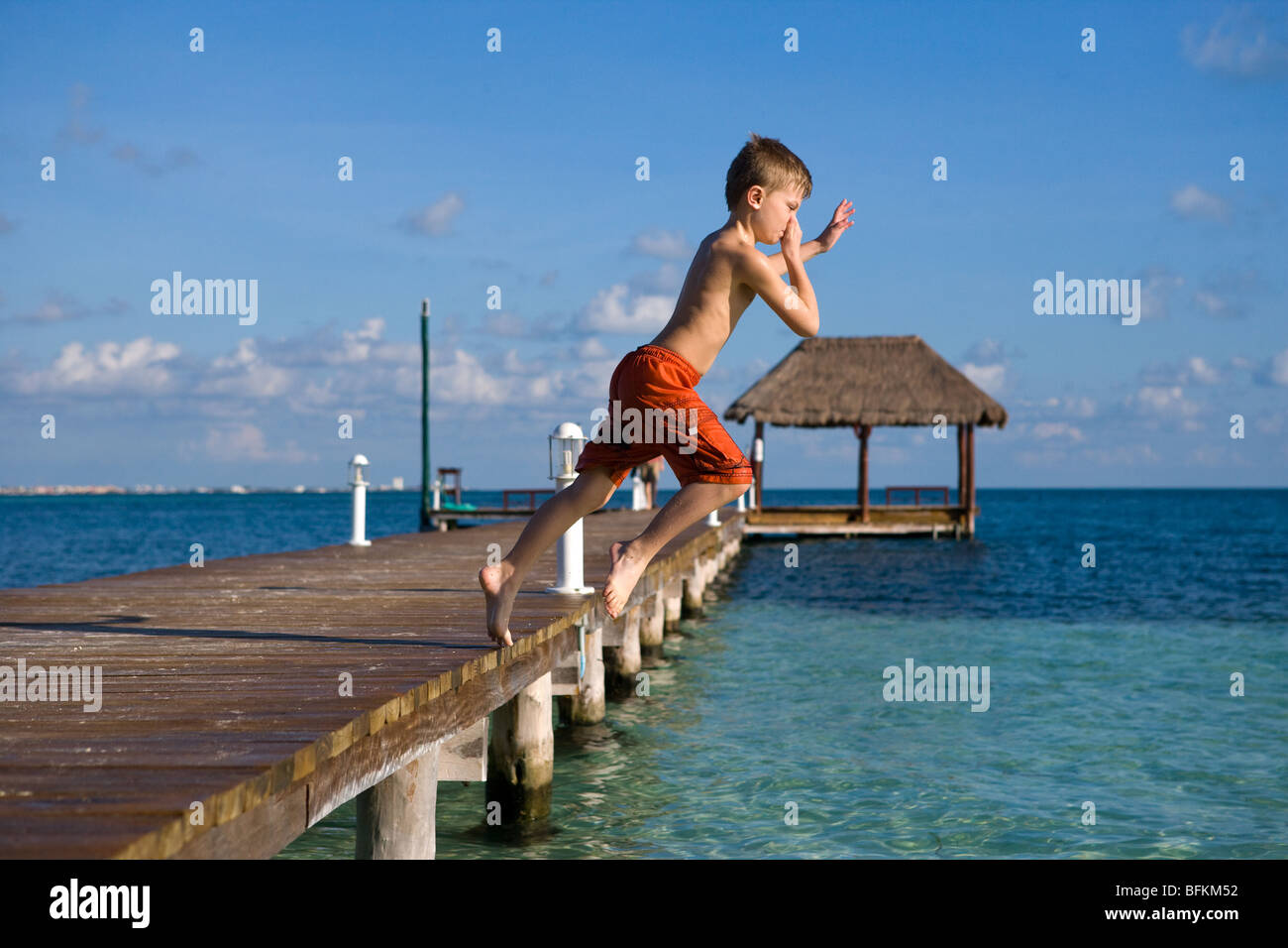 A Small Boy Jumps off a Dock at Club de international Cancun Mexico into the tropical waters off the Yucatan Stock Photo