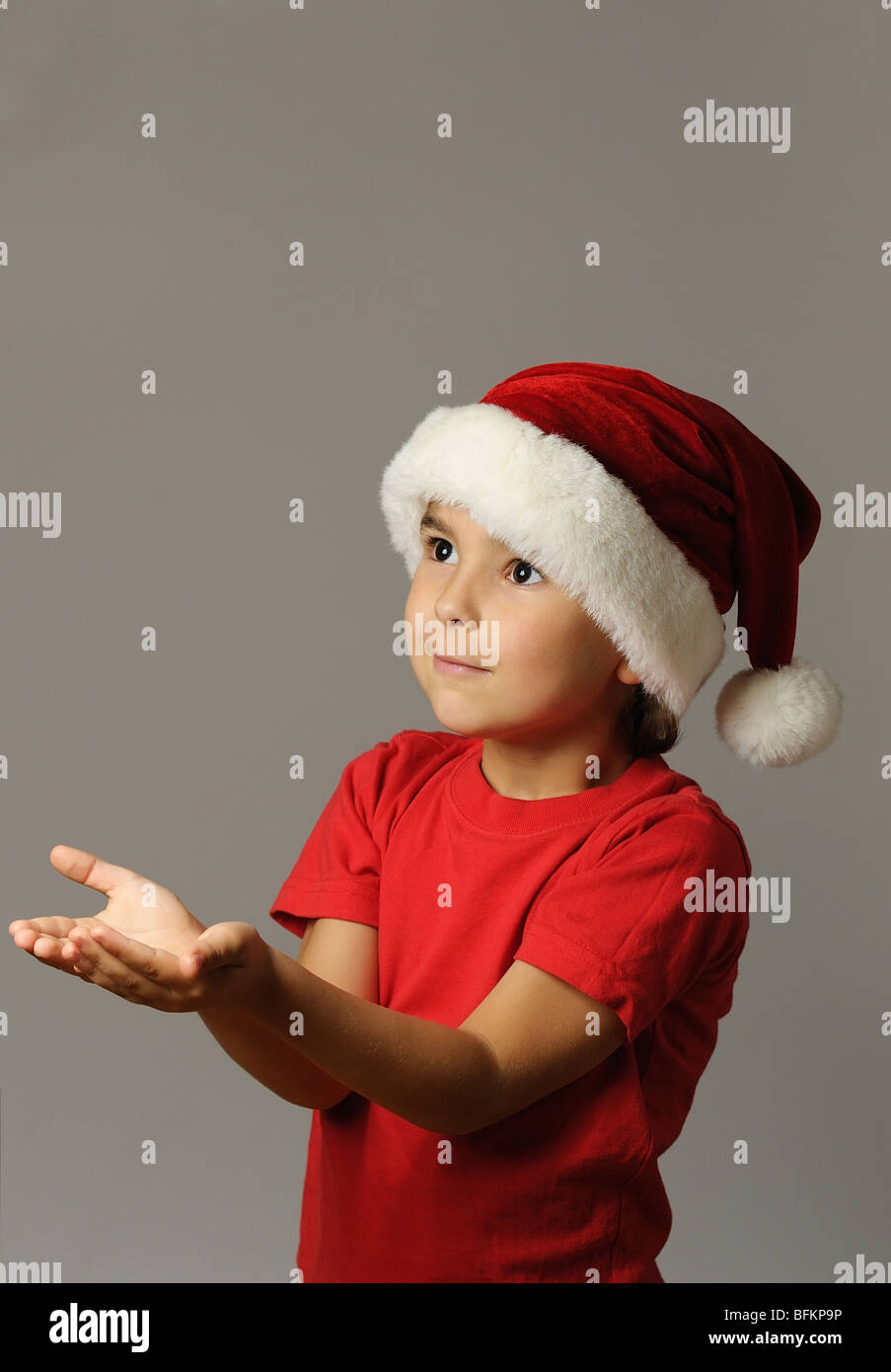 Kid in Santa hat and red t-shirt holding an imaginary gift Stock Photo