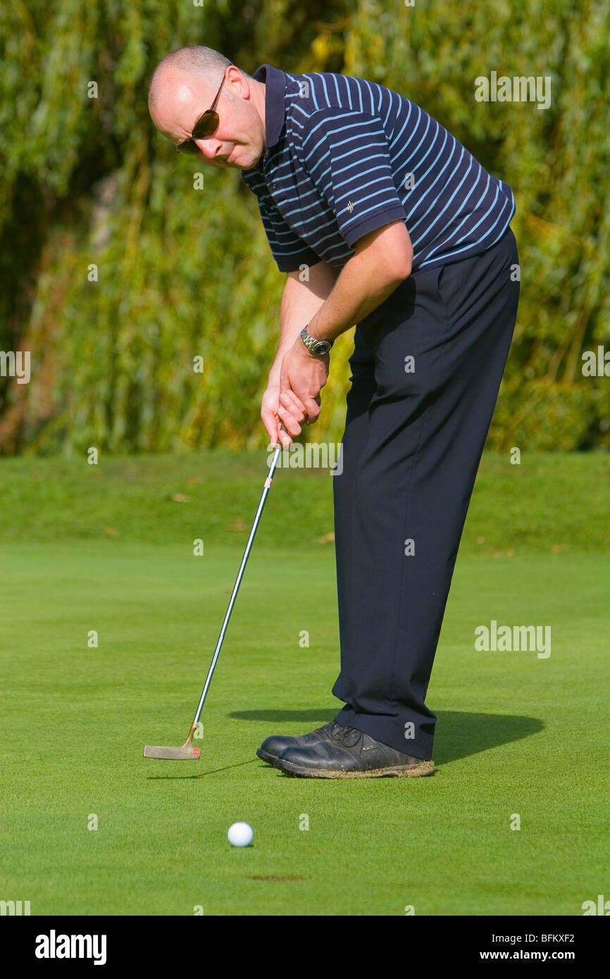 A middle aged white male golfer watching his ball on its way to the hole while putting on the green Stock Photo