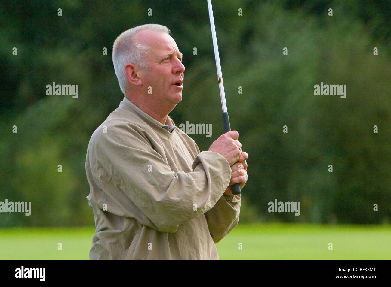 A middle aged white male playing golf watching his ball after taking a shot from the fairway Stock Photo