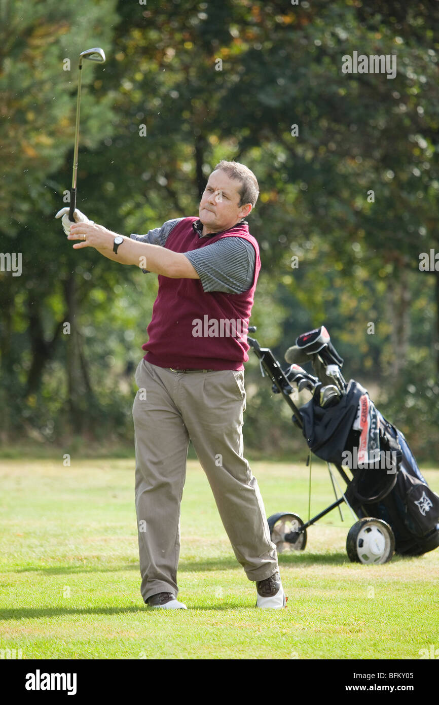 A white male playing golf and taking a shot from the fairway with an iron Stock Photo