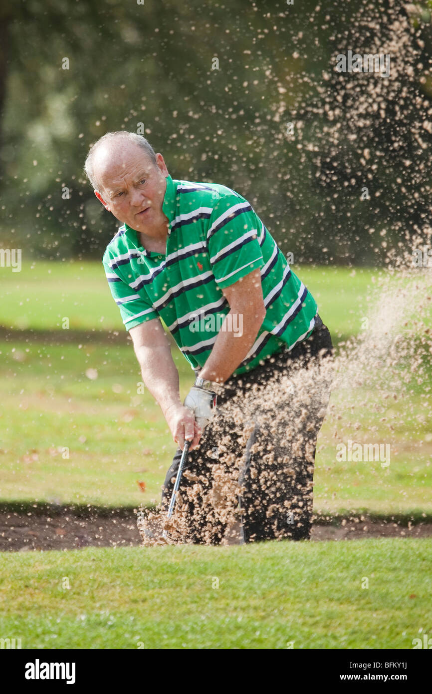 A white male playing golf and taking a shot from a sand bunker Stock Photo