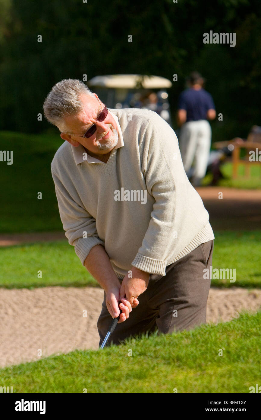 A middle aged white male playing golf and taking a shot from a sand bunker Stock Photo
