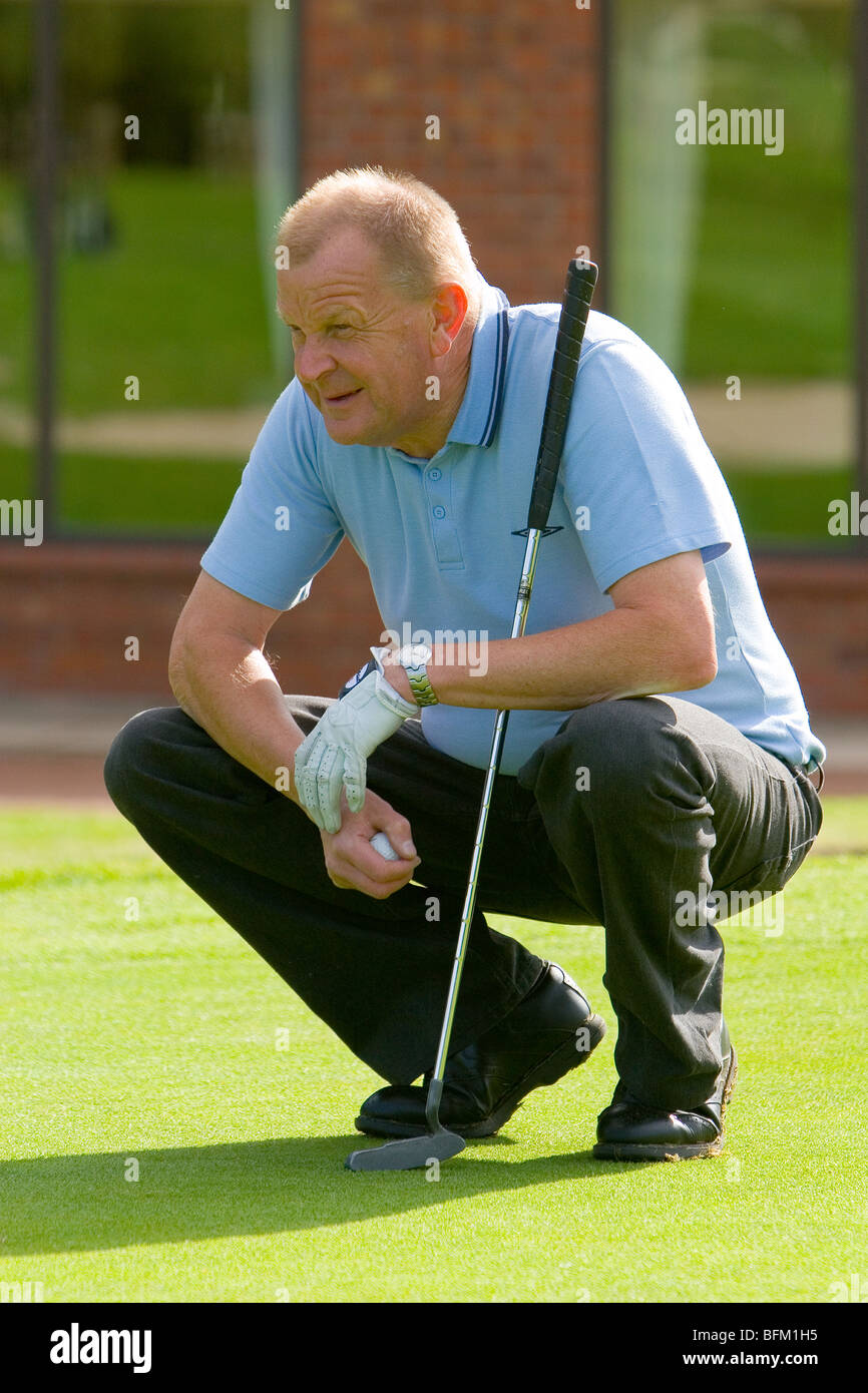 A middle aged white male preparing to line up his shot on the green while holding his putter and golf ball Stock Photo