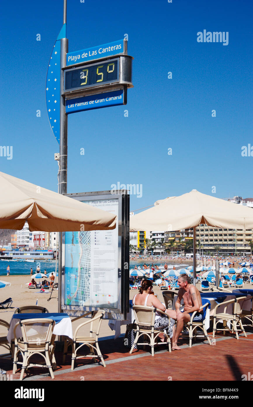 Couple at outdoor cafe overlooking Playa de Las Canteras in Las Palmas on Gran Canaria. Temperature guage showing 35 degrees. Stock Photo