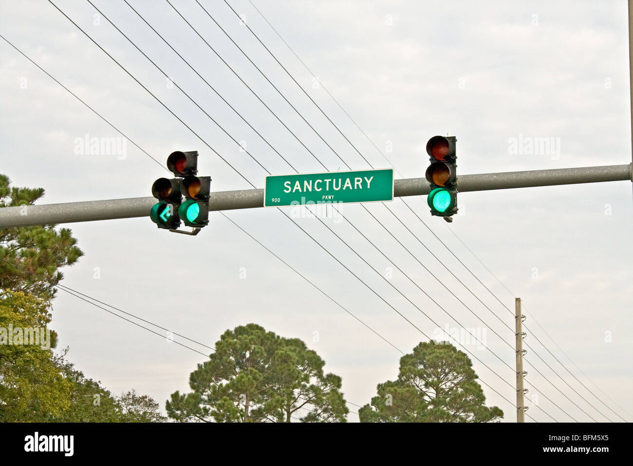 Green stoplights and arrow pointing towards a street called Sanctuary in Jacksonville Beach, Florida with power lines Stock Photo