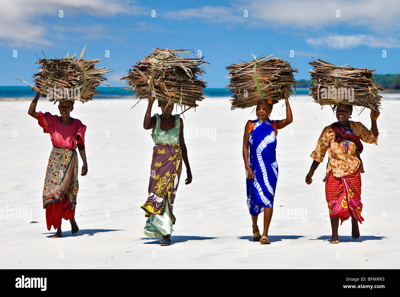 Kenya Mombasa. Women carry on their heads makuti (dried coconut palm fronds used as roofing material) on Kenya s south coast. Stock Photo