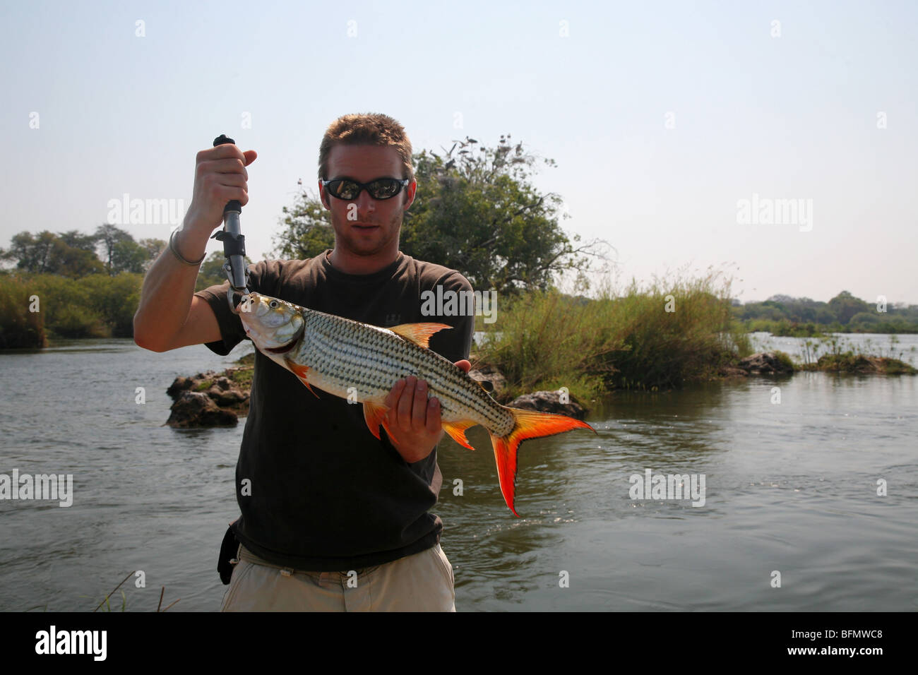 Botswana, Zambezi river. A young man proudly shows off his catch; a