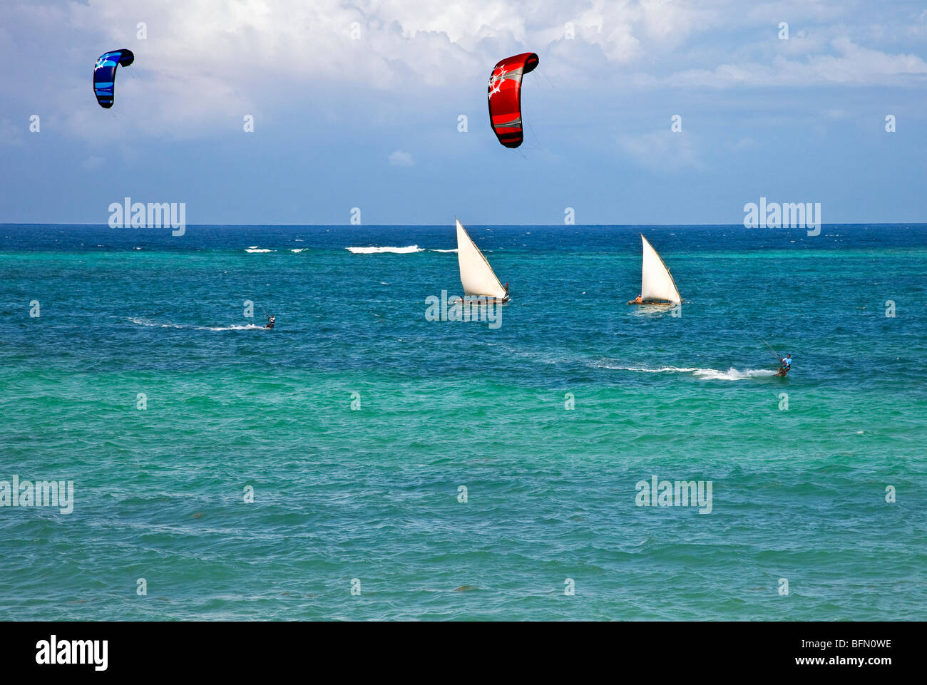 Kenya, Mombasa. Two kite surfers speed away from outrigger canoes sailing in the clear waters of Diani Beach. Stock Photo