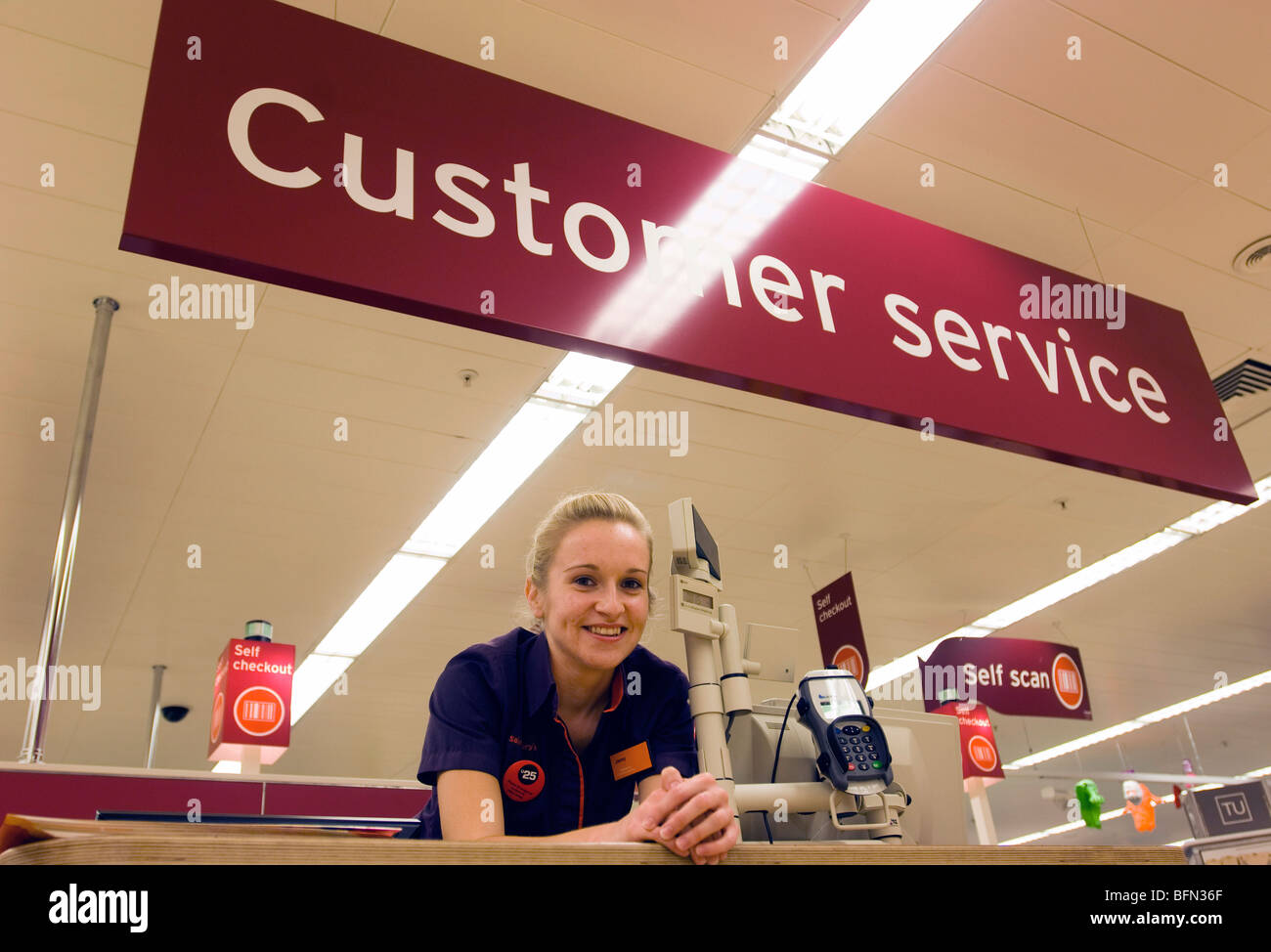 Sainsbury's supermarket girl in uniform at a customer service desk in a store. Stock Photo