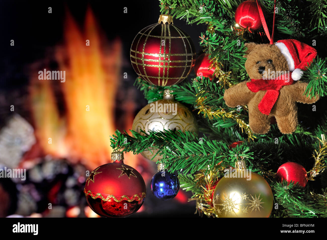 Teddy bear and bells hanging in Christmas tree in front of hearth / fireplace Stock Photo