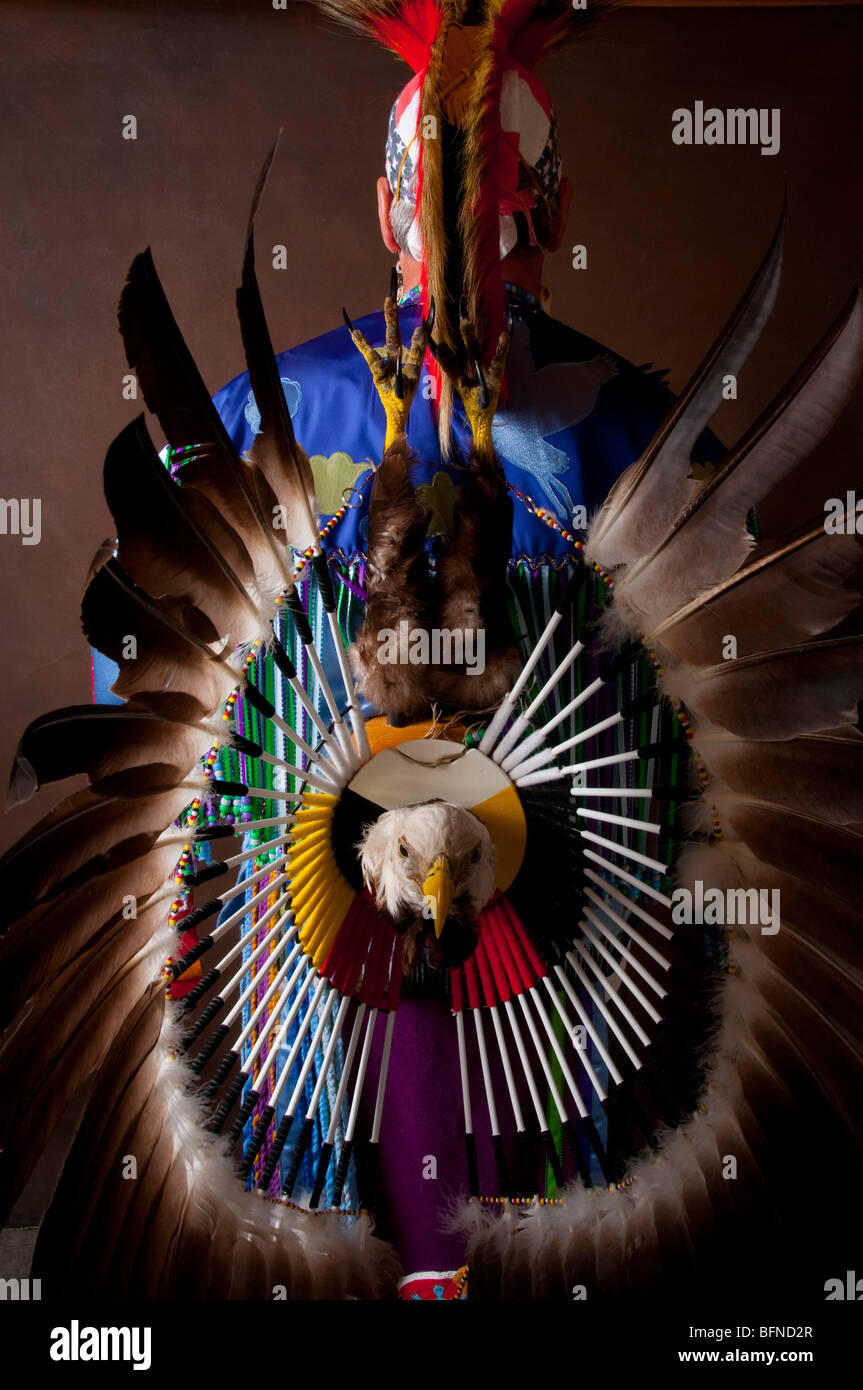 Native American Indian Male in full regalia with Eagle head feathers legs and talons on bustle of costume on brown background Stock Photo