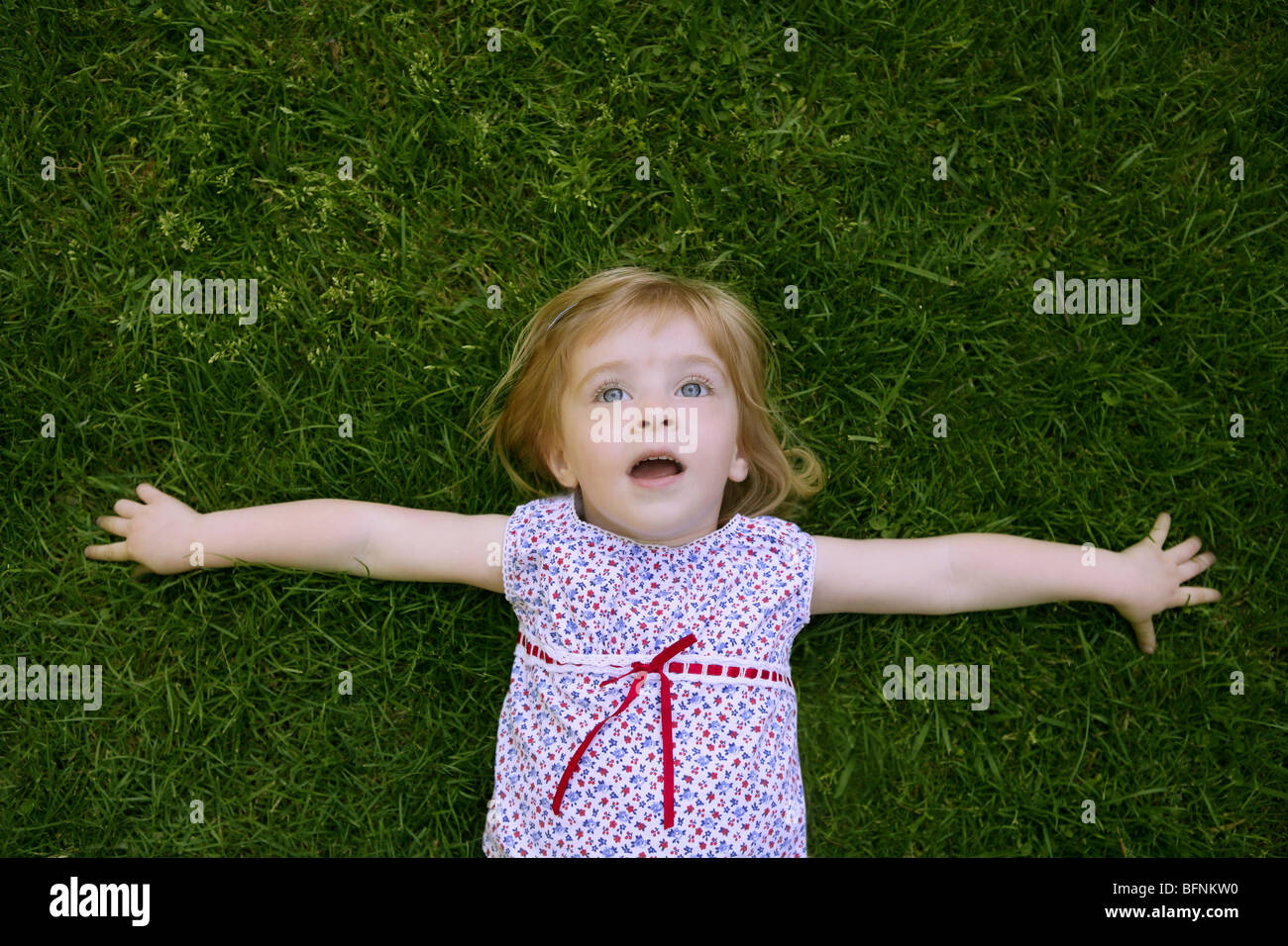 Beautiful little toddler girl happy lying on the green grass Stock ...
