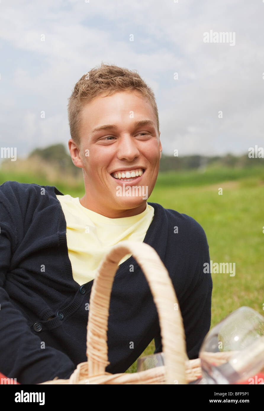 Young smiling man lying on the grass with picnic basket near him Stock