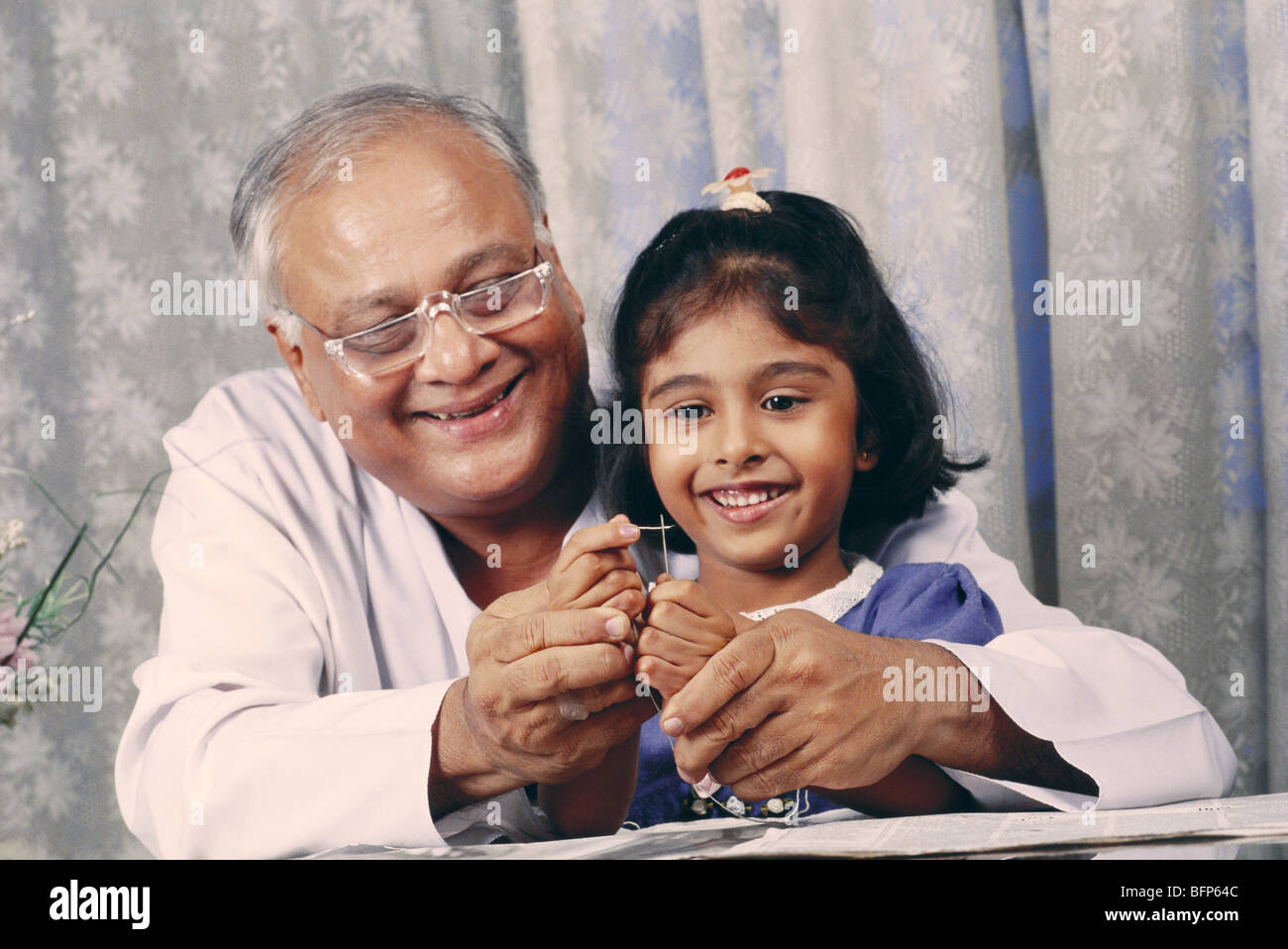 Indian senior Grandfather teaching granddaughter threading of needle ; india ; asia ; MR320;322