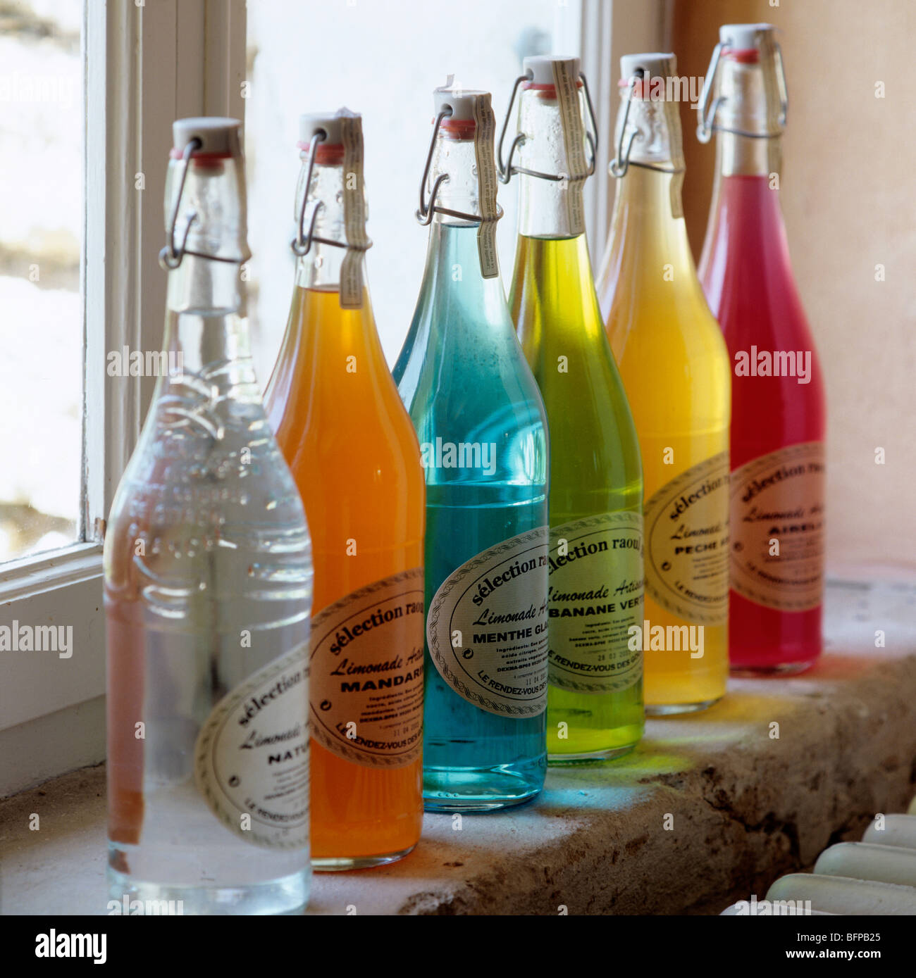 Row of glass bottles filled with multicoloured liquids on windowsill / ledge Stock Photo