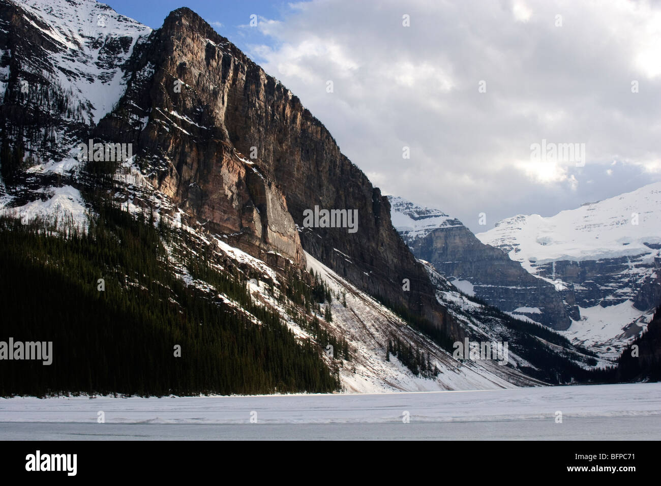 Lake Louise before the spring thaw.  Ice on the Lake and snow on the mountain with sunshine peaking through with a hint of blue Stock Photo