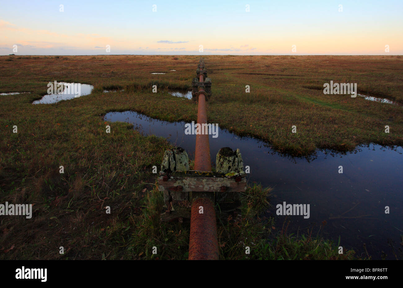 A rusty pipeline stretches out into the distance across the salt marshes at Stiffkey. Stock Photo
