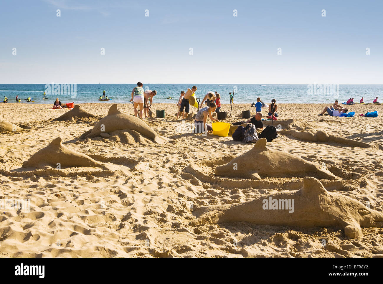 Families making sand sculptures of dolphins on Boscombe beach, Bournemouth, Dorset. UK. Stock Photo