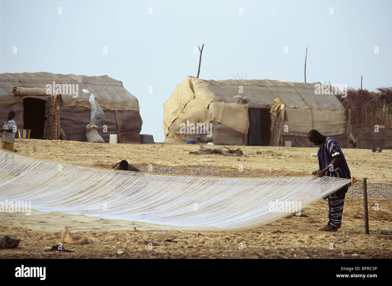 Bozo fisherman checks his nets on the banks of the Niger River with traditional cottages in the background Stock Photo