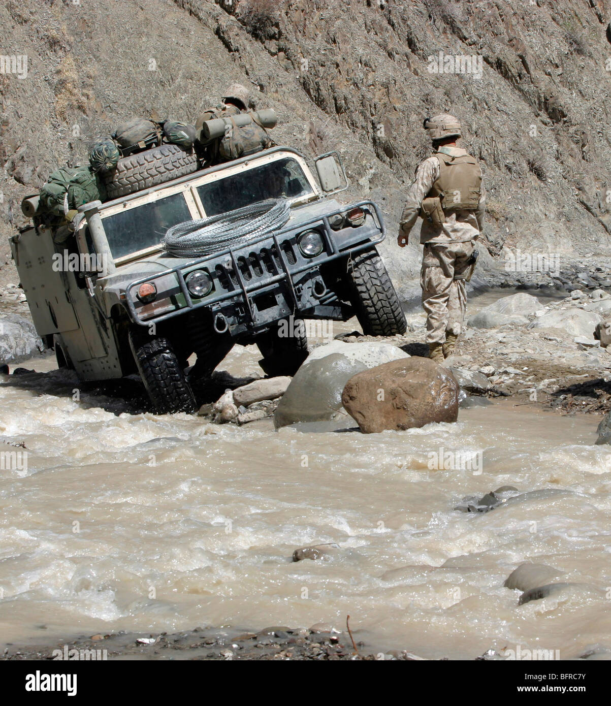 A U.S. Marine guiding the driver of a Humvee through a river in Khowst Province of Afghanistan. Stock Photo