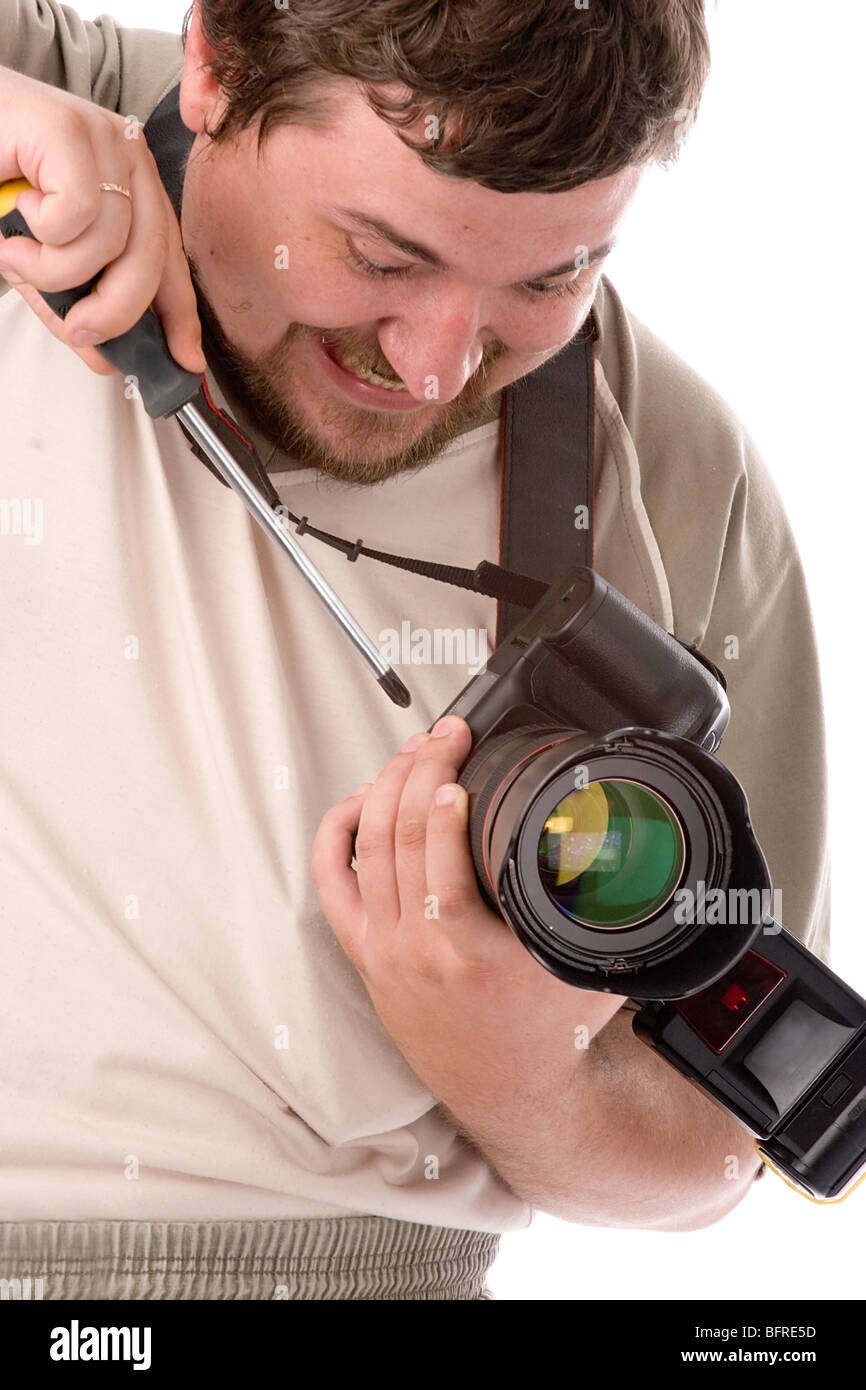 man with terrible facial expression and big screwdriver in hands fixing new DSLR camera Stock Photo