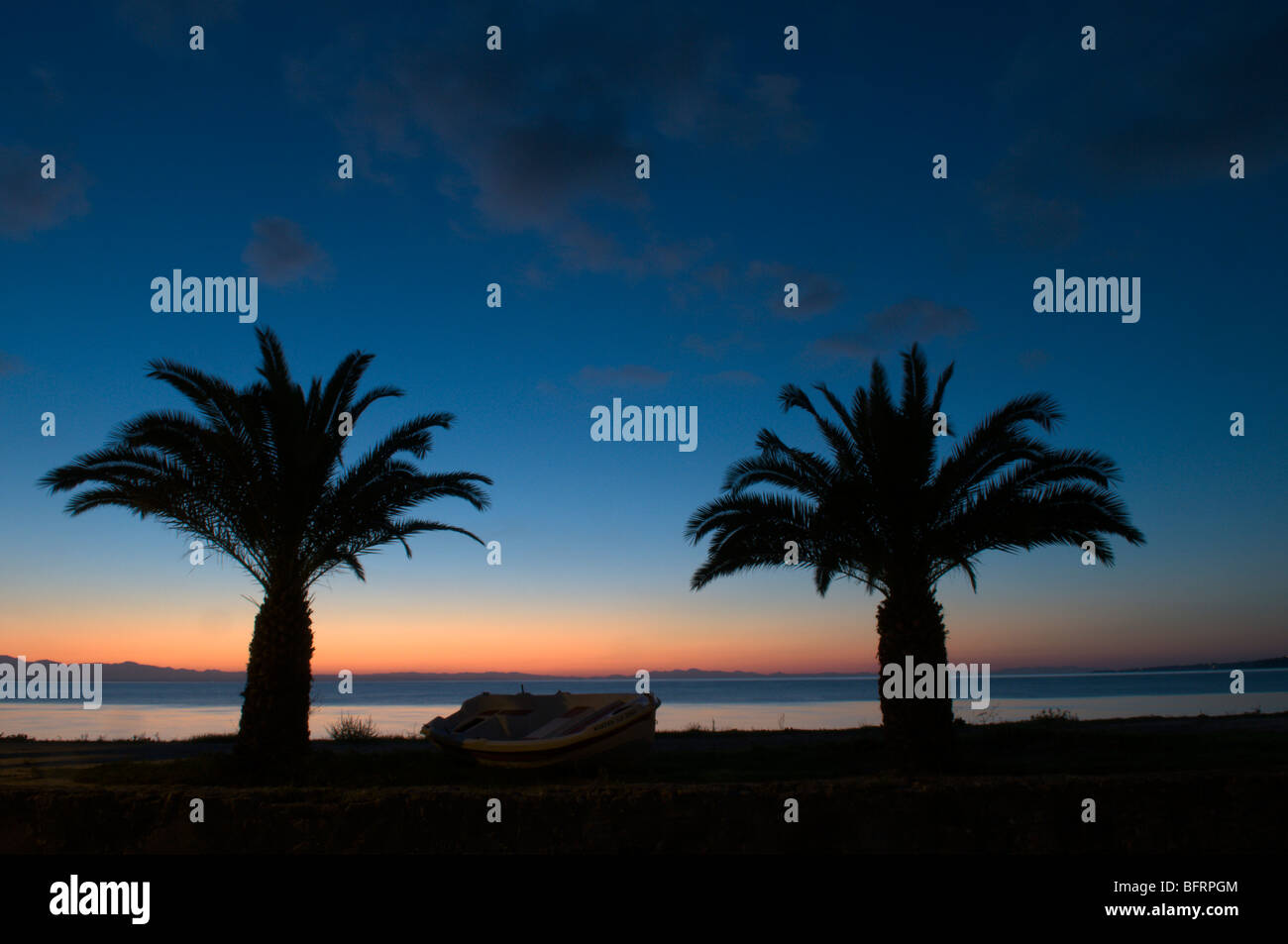 Greece. Zakynthos. Zante. Greek island. October. Colourful sunrise seen through palm trees on the road north out of Zakinthos Town to Krioneri. Dawn. Stock Photo