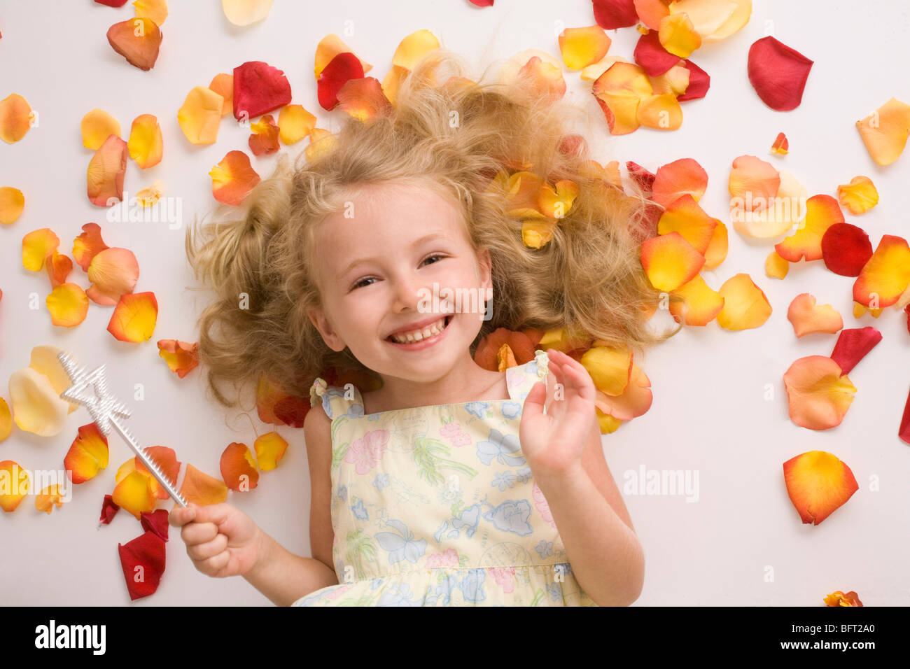 Blond Girl with Magic Wand Lying Amongst Flower Petals Stock Photo