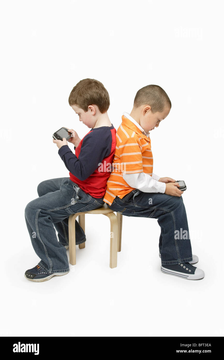 Boys with Handheld Video Games Sitting Back to Back Stock Photo