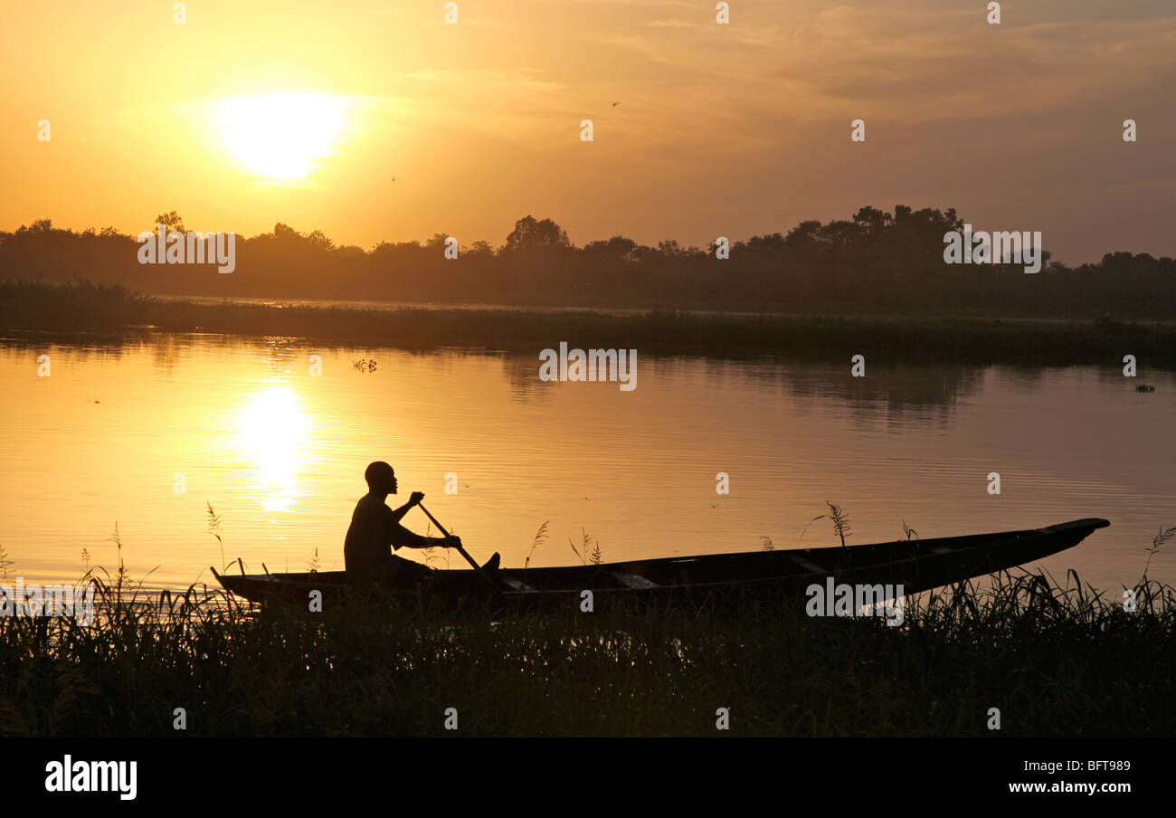 Fisherman in a small boot crossing a river at sunset Stock Photo