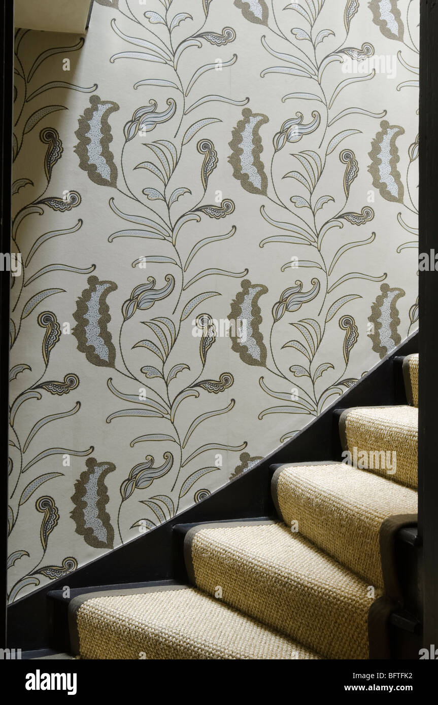 Seagrass carpeted staircase with floral leafy print wallpaper. Stock Photo