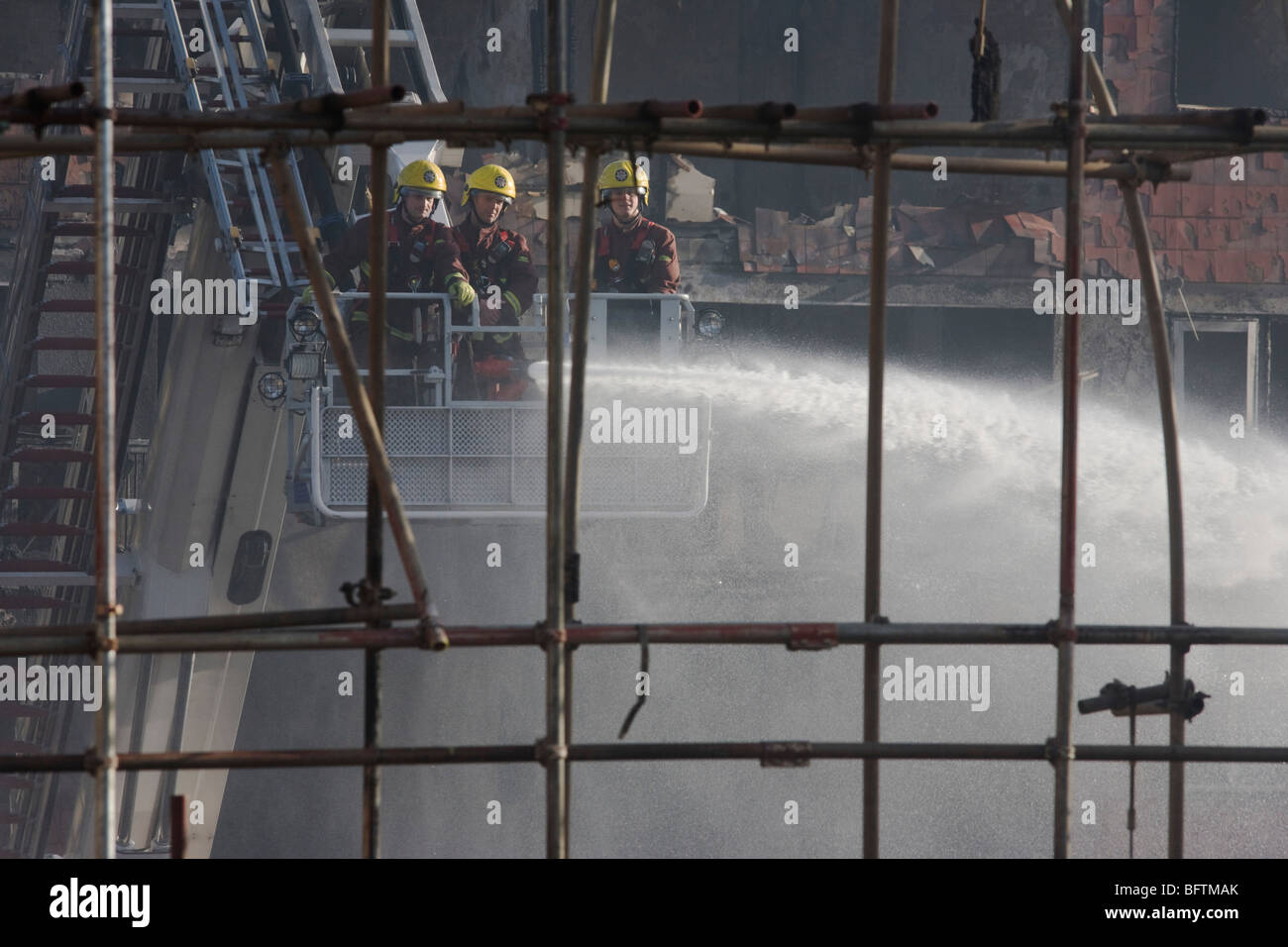 London Fire fighters dampen down smouldering remains from a Simon Snorkel platform after an inner-city estate fire in London Stock Photo