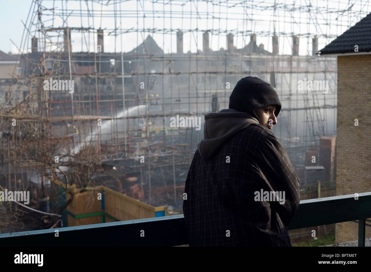 Young hoodie looks at the devastation of a construction site after an inner-city estate fire in south London. Stock Photo