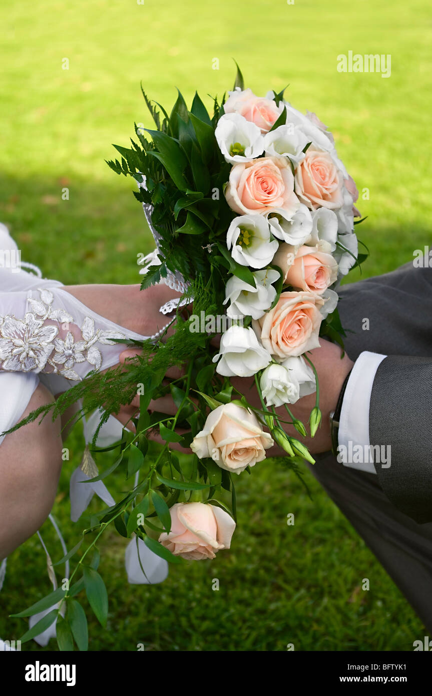Bride and groom hold bouquet of flowers in hand. Cropped by hands Stock