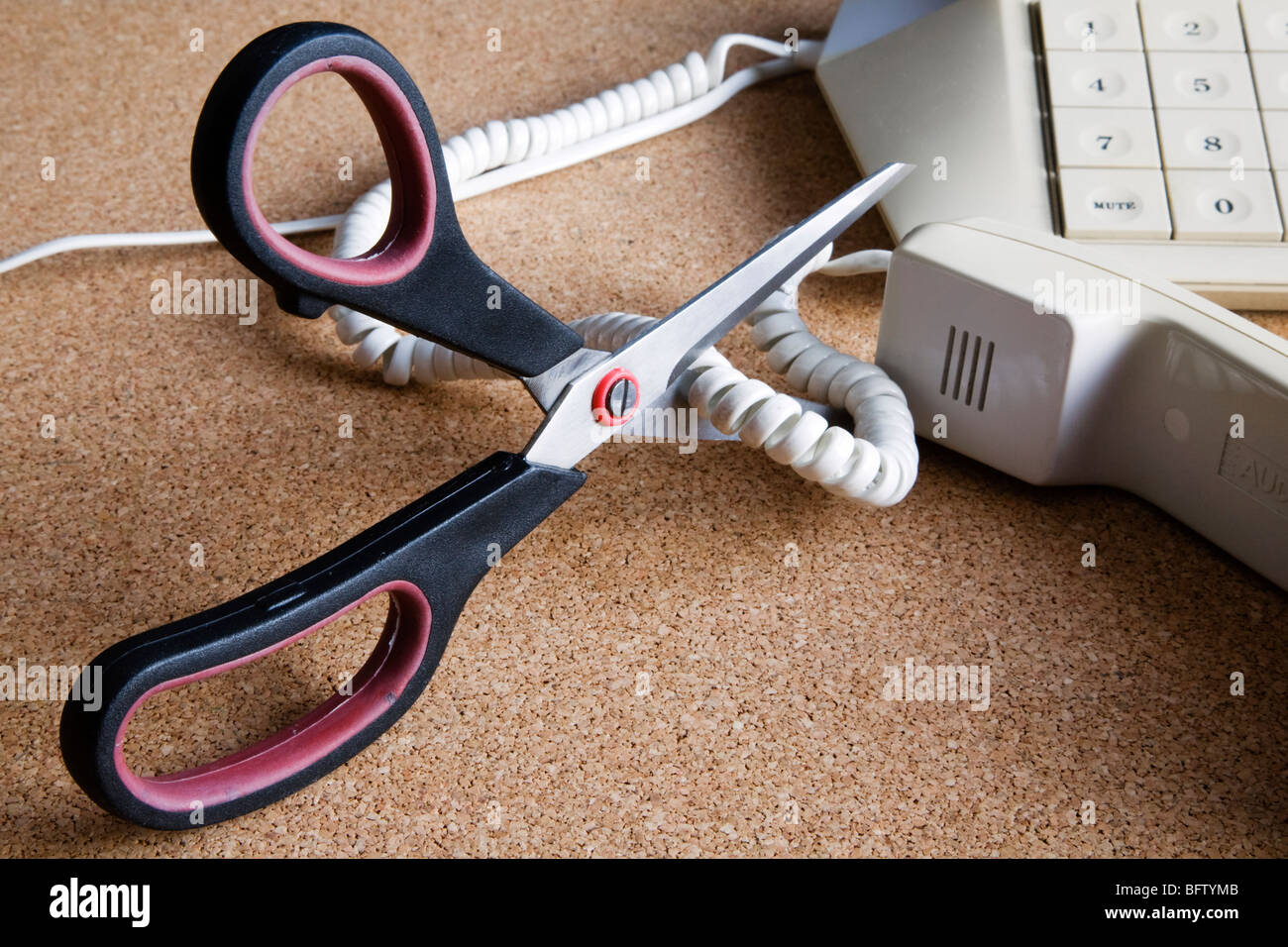 A pair of scissors cutting through a telephone cord. Stock Photo