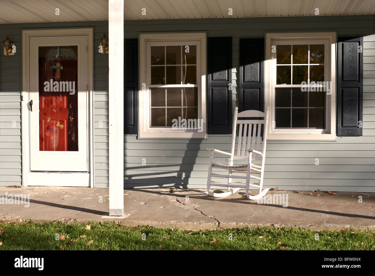 red entry door & charming front porch with white wood rocking chair old gray clapboard house on autumn day Montgomery New York Stock Photo