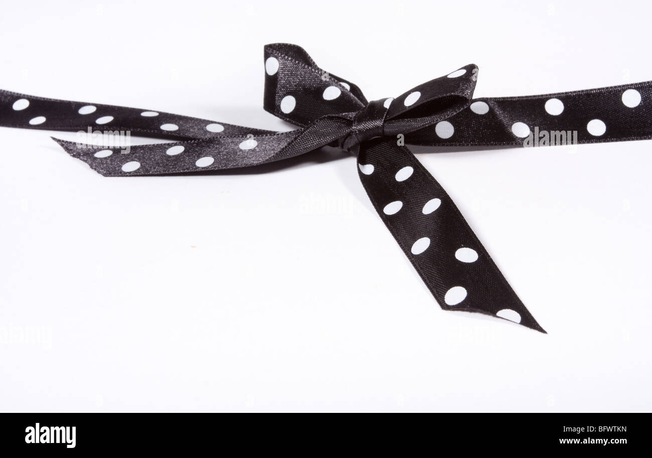 Black and white Polka Dot Ribbon tied in a bow over white card used to wrap up a xmas, birthday or valentine present etc... Stock Photo