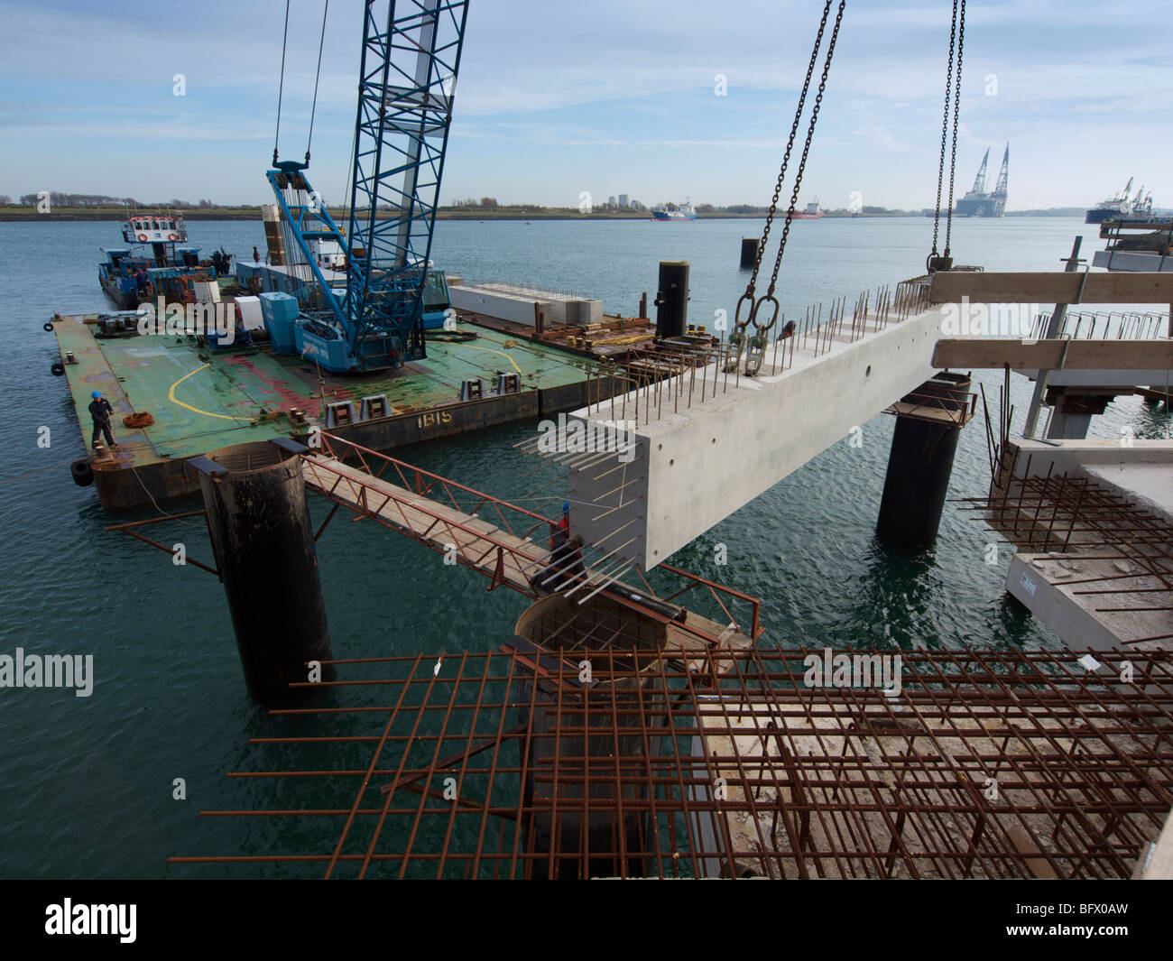 Large floating crane lifting a concrete block into place while building a docking station pier for a large petroleum ship. Stock Photo