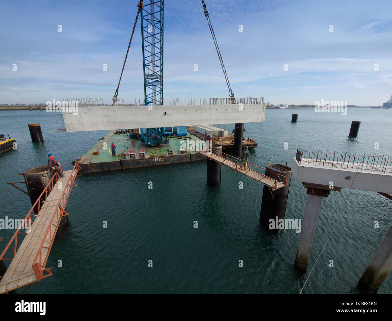 Large floating crane lifting a concrete block into place while building a docking station pier for a large petroleum ship. Stock Photo