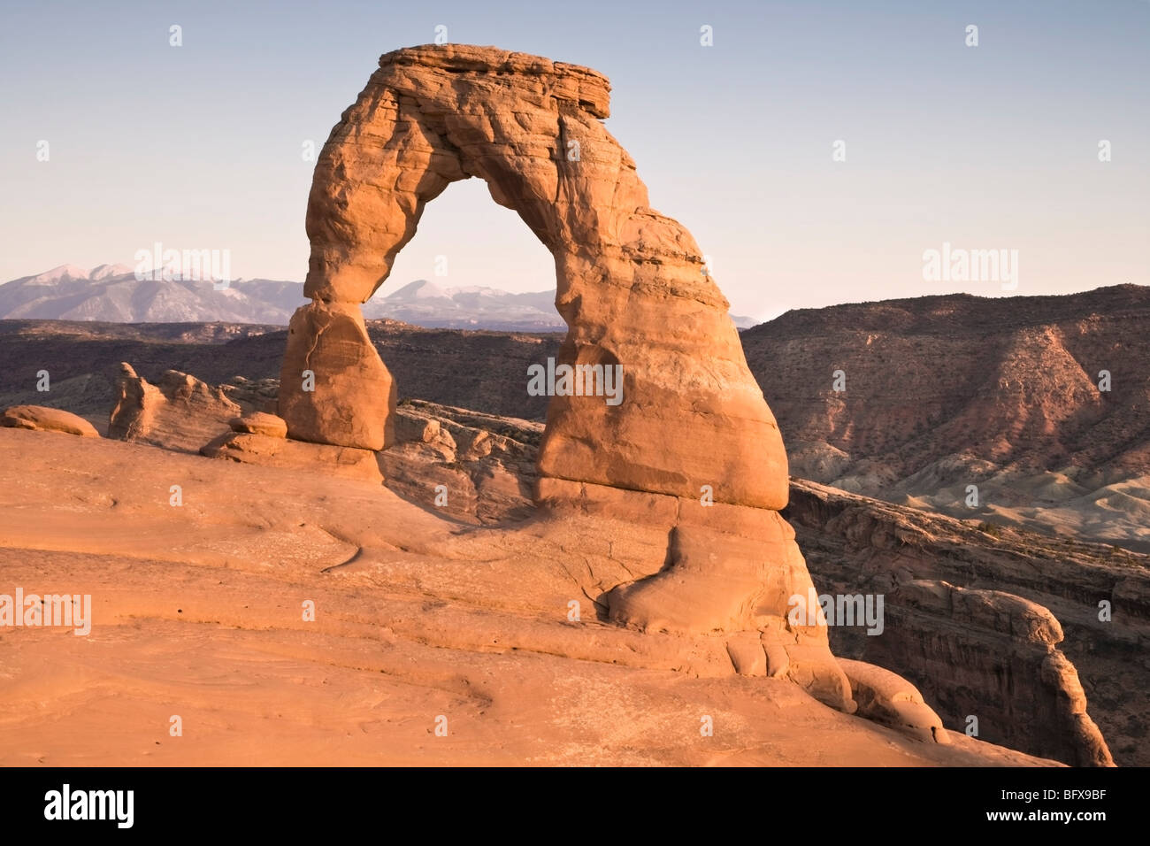 Delicate Arch at Arches National Park at Sunset with mountain range in the background Stock Photo