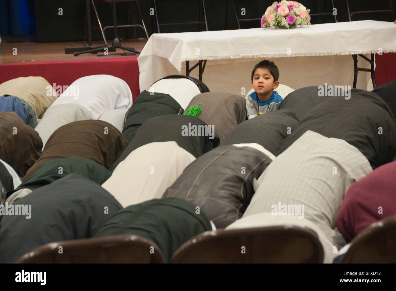 Boyr with men prostrated at prayers at Eid Milad-Un-Nabi Celebrations at Sunni Muslim Association, Tooting, London. Stock Photo