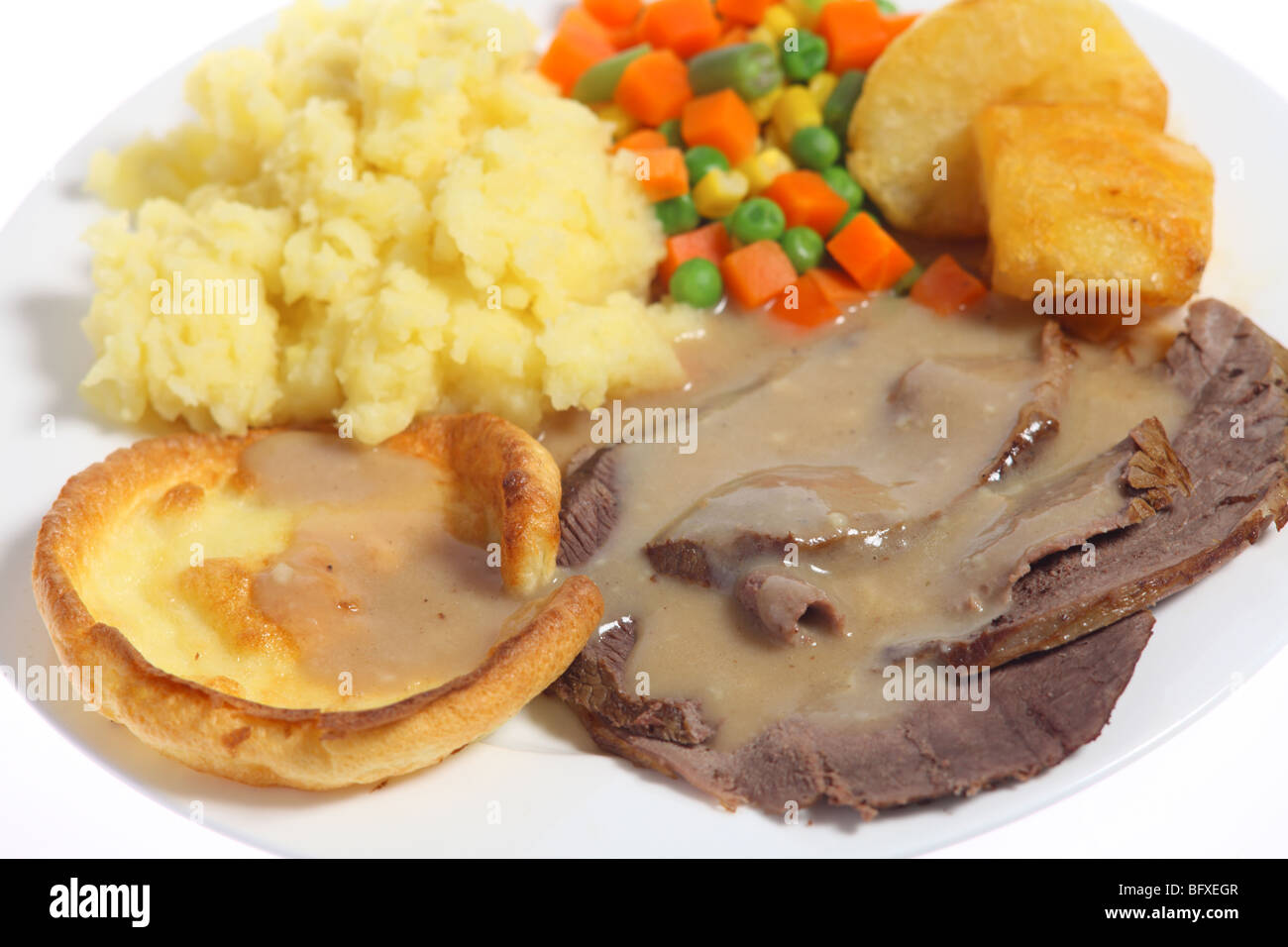Close-up on a plate of roast beef, yorkshire pudding (or popover), diced vegetables and potato. Stock Photo