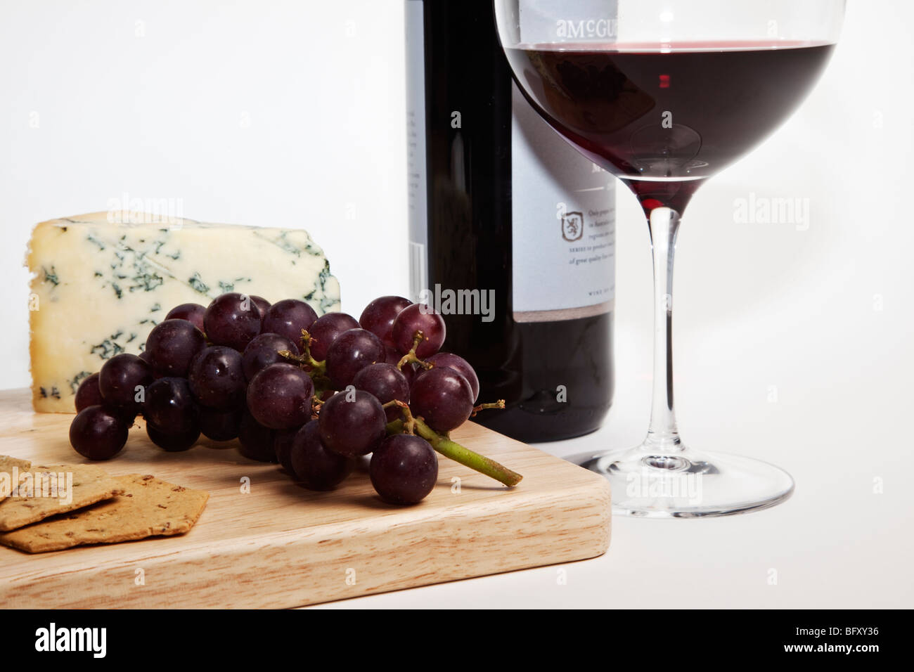 Stilton with red grapes and crackers on a wooden cheese board accompanied by a bottle and glass of red wine. Stock Photo