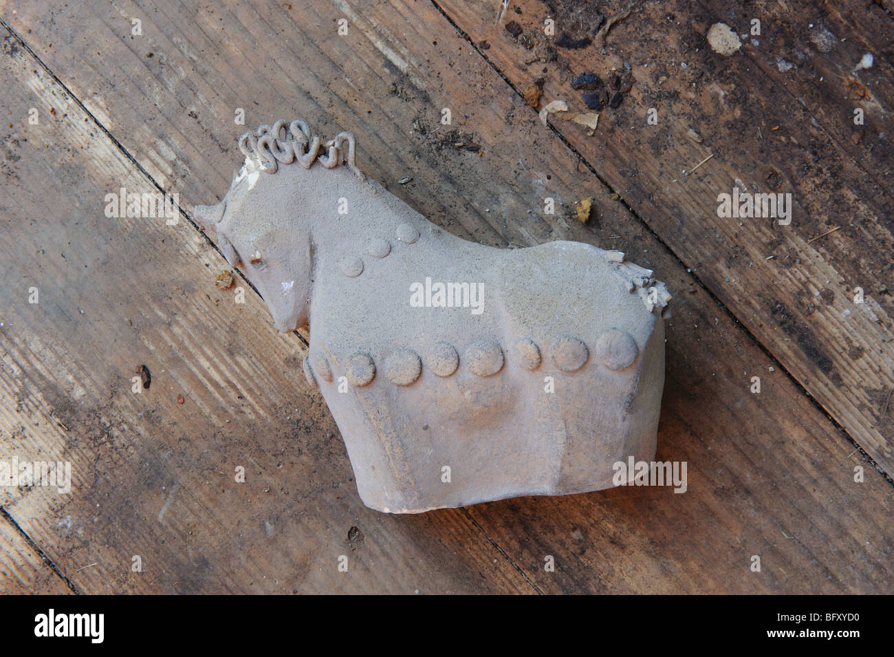 Unfinished, unglazed and broken ceramic horse ornament lies on dirty wooden floor Stock Photo