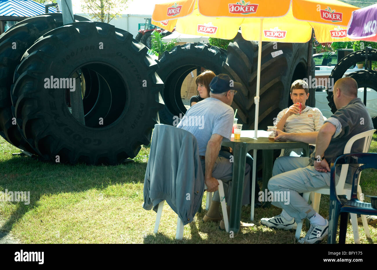 Undeterred by giant-sized tyres on display, visitors to a Gascony agricultural fair relax over refreshments Stock Photo