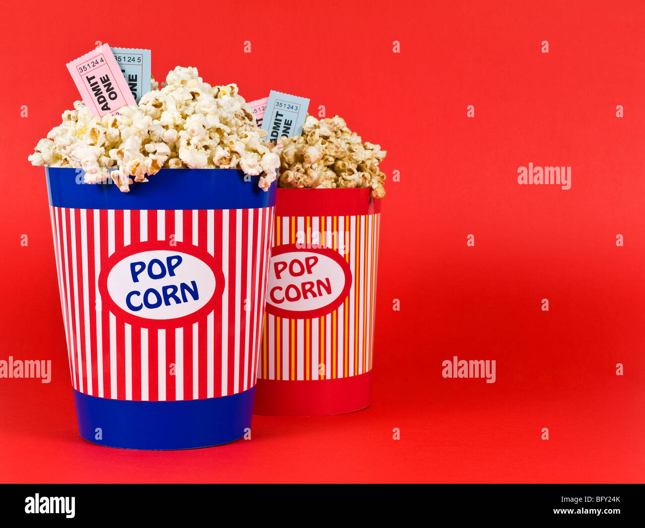 Two popcorn buckets over a red background. Movie stubs sitting over the popcorn. Stock Photo