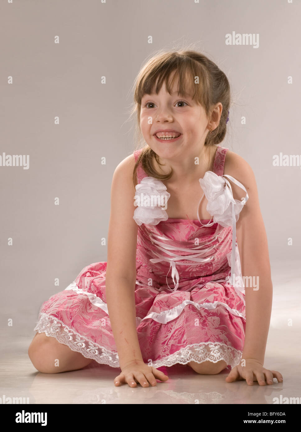 Beautiful little girl in pink dress sits on the floor and laughs ...