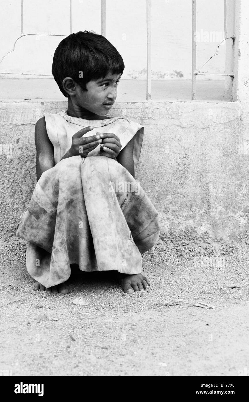 Young poor Indian girl leaning against a wall, alone on the street, in rural  India with copy space Stock Photo