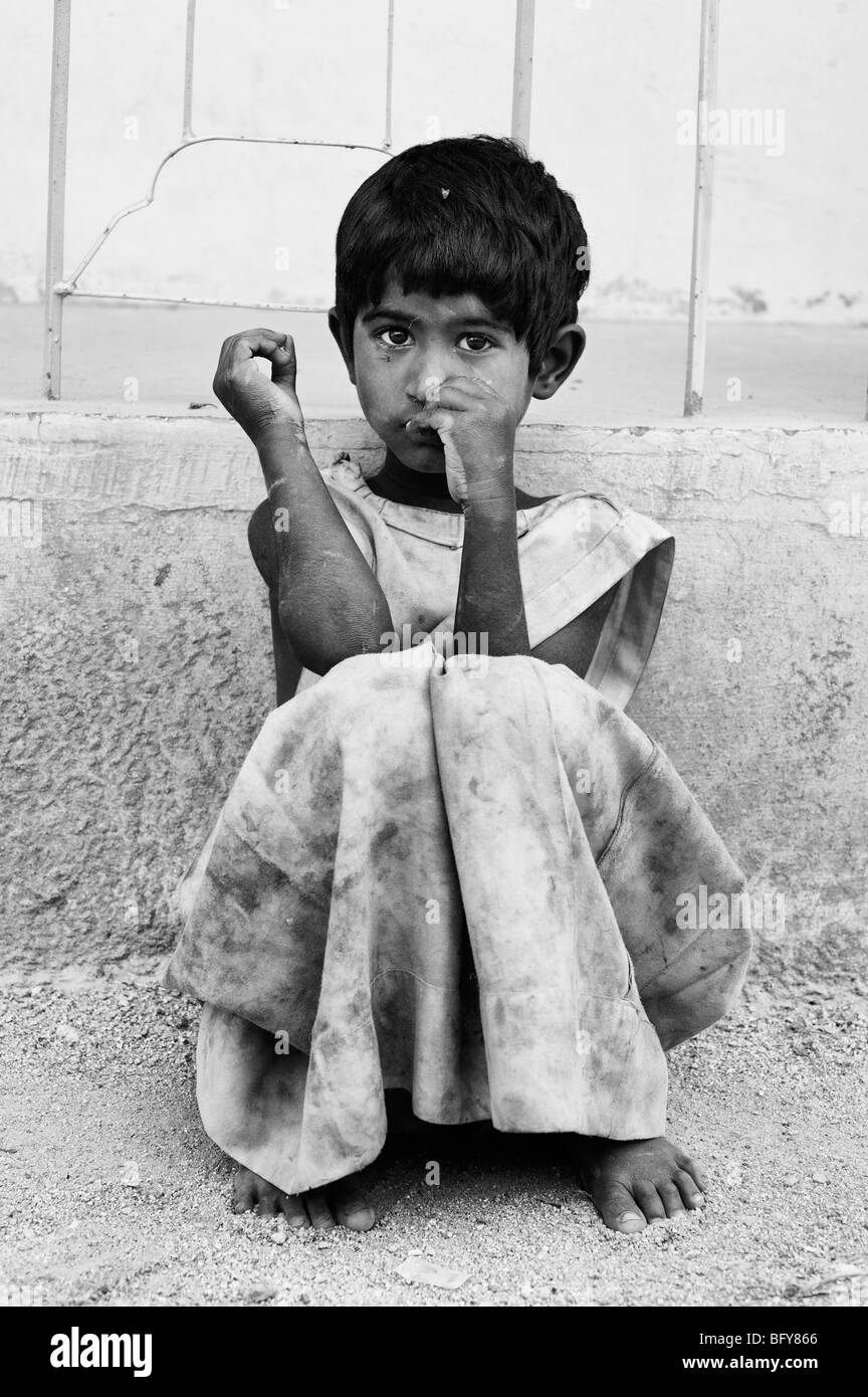 Young poor Indian girl leaning against a wall, alone on the street, in rural  India. Black and White Stock Photo
