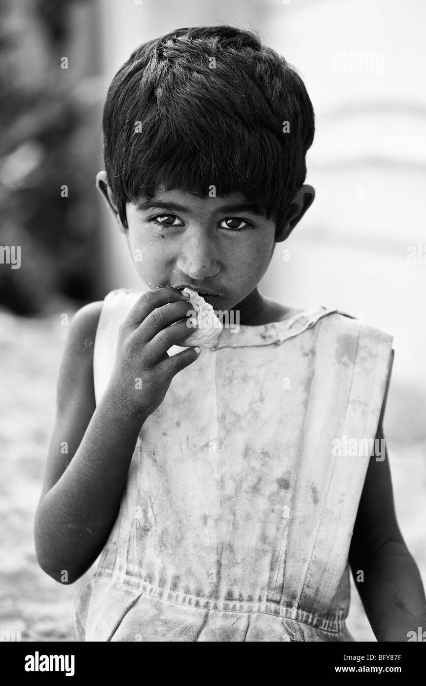 Young poor Indian street girl eating a biscuit in a street in India. Black and white selective focus Stock Photo